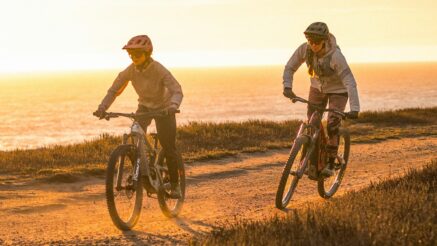 Two people riding eBikes on a mountain bike trail by the beach.
